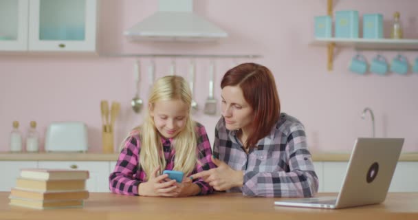 Ung voksen kvinde og smuk pige ser video på mobiltelefon ansøgning. Familie har det sjovt at surfe på internettet sammen. Mor og datter bliver hjemme. – Stock-video