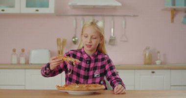 Pembe tişörtlü şirin kız pembe mutfakta pizza yiyor. Liseli kız elleriyle pizza yemekten hoşlanır. Evdeki aç çocuk..