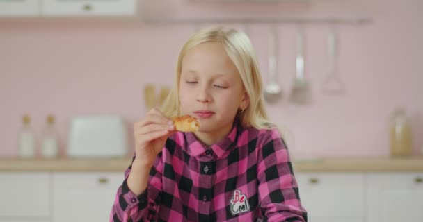 Портрет милої дівчинки-блондинки в рожевій сорочці, що їсть піцу руками на рожевій кухні. Голодній школярці подобається їсти піцу з плавленим сиром . — стокове відео