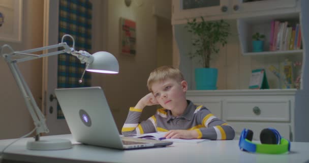 El niño preescolar está cansado de estudiar en línea en casa. Educación en línea y aprendizaje a distancia para niños. Joven niño escuchando a profesor asignación en el ordenador portátil. — Vídeos de Stock