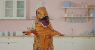 Kahverengi dinozorun pembe mutfakta komik dansı. Dinozor maskotunun komik hareketleri. Yavaş çekim eğlenceli dans.