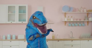 Pembe mutfakta mavi dinozorun komik dansı. Dinozor maskotunun komik hareketleri. Yavaş çekim eğlenceli dans.