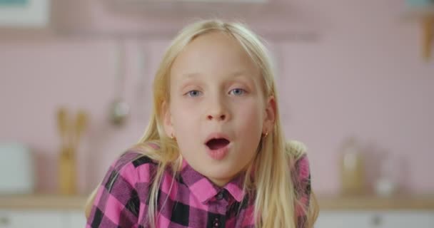 Aranyos szőke iskolás lány portréja, ahogy beszél és a kamerába néz. 10 éves lány rózsaszín ingben beszél a kamera előtt. — Stock videók