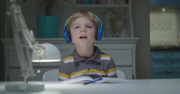 Niño en edad preescolar en color auriculares inalámbricos cantando mirando a la cámara. Webcam vista de niño que habla. Educación en línea y aprendizaje a distancia para niños. — Vídeos de Stock