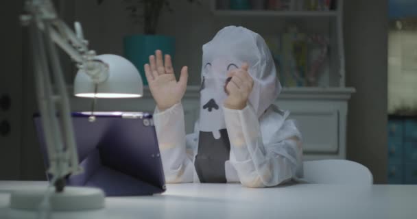 Child in halloween ghost costume talking by video call on tablet computer. Quarantine halloween celebration. — Stock Video