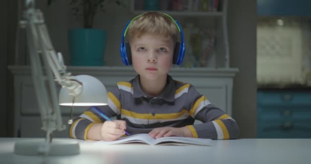 Niño de edad elemental en auriculares de color que estudian en línea en casa. Webcam vista de niño pequeño escribiendo y hablando con el profesor en línea. Educación en línea y aprendizaje a distancia para niños. — Vídeo de stock