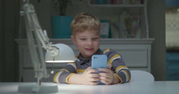 Menino pré-escolar usando aplicativo de telefone celular e fazendo caras engraçadas para câmera móvel frontal. Criança brincando com divertido aplicativo de telefone celular. — Vídeo de Stock