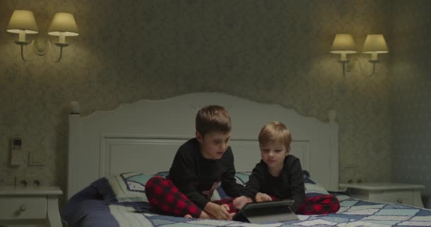 Los hermanos usan la tableta para la película antes de acostarse. Dos niños jugando en la computadora de la tableta. Dos hermanos usando una tableta. — Vídeo de stock