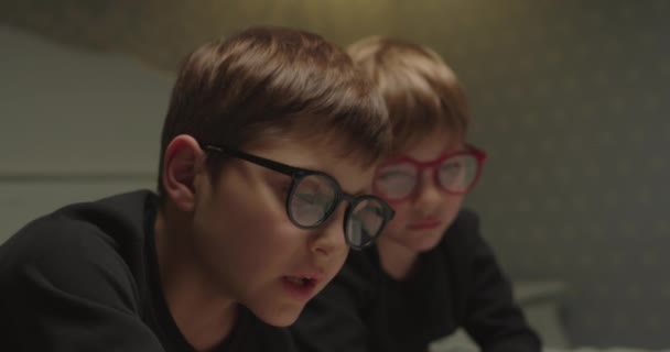 Testvérek szemüveg olvasás papír könyvet. Közelkép fiúkról, akik mesét olvasnak lefekvés előtt. Szemészeti problémákkal küzdő gyermekek. — Stock videók