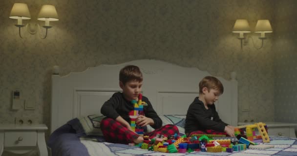 Frères et sœurs jouant ensemble assis sur le lit. Enfants avec des blocs de construction en plastique de couleur à la maison. Temps libre le soir. — Video