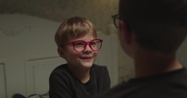 Kleurige jongen met een rode bril die met zijn broer voor hem zit te praten. Schouder uitzicht van lachend kind praten met vriend. — Stockvideo