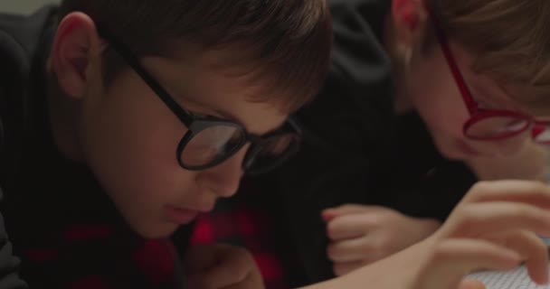 Geschwister mit Brille lesen Papierbuch. Großaufnahme von Jungen, die vor dem Schlafengehen Märchen lesen. Kinder mit Sehproblemen. — Stockvideo