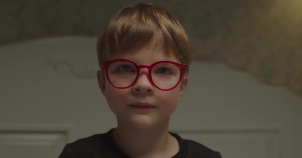 빨간 눈 안경을 쓴 행복 한 아이가 카메라를 보고 있습니다. 안경쓴 매력적 인 소년의 초상화. 시력 문제가 있는 어린이들. — 비디오
