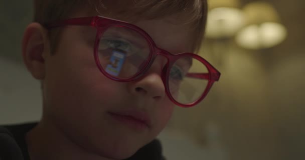 Närbild av barn ansikte i röda glasögon surfa internet med mobiltelefon skärm reflektion i glasögon. Söt pojke sms på smartphone. — Stockvideo