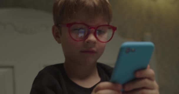 Lindo niño preescolar en gafas para los ojos utilizando el teléfono móvil para navegar por Internet en línea. Retrato de niño sosteniendo teléfono inteligente. De cerca.. — Vídeo de stock