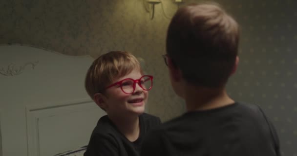 Niño lindo preescolar en gafas rojas hablando con su hermano sentado frente a él. Vista del hombro de un niño sonriente hablando con un amigo. — Vídeo de stock