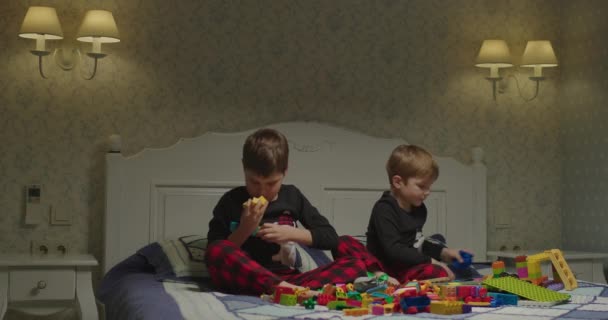 Two kids playing with color plastic building blocks. Brothers spend time together at home. Bedtime games.