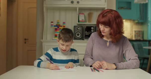 Kind mit Autismus malt mit Buntstiften, wobei ihm die Mutter hilft. Aufklärung über Autismus-Spektrum-Störungen zu Hause. Mutter als Autismus-Therapeutin. — Stockvideo