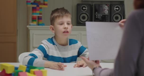 Niño autista aprendiendo emociones con tutor. El profesor muestra papel a los alumnos con autismo. Terapeuta de análisis de comportamiento aplicado que trabaja con un niño. — Vídeo de stock