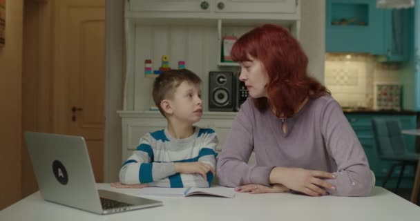 Mamá ayudando a su hijo con autismo a hacer los deberes para la escuela en línea. Educación en el hogar por Internet. Educación sobre el trastorno del espectro autista en el hogar. — Vídeo de stock