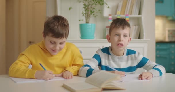 Två pojkar med autism har skrivlektion sittande vid bordet. Hemundervisning för barn under karantänen. — Stockvideo
