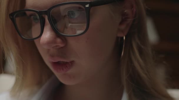 ラップトップで入力する若い20代の女性の閉じます。眼鏡の女子学生がエッセイを書く。家庭での千年紀の勉強。笑顔ブロンド女性作業で目ガラス反射. — ストック動画