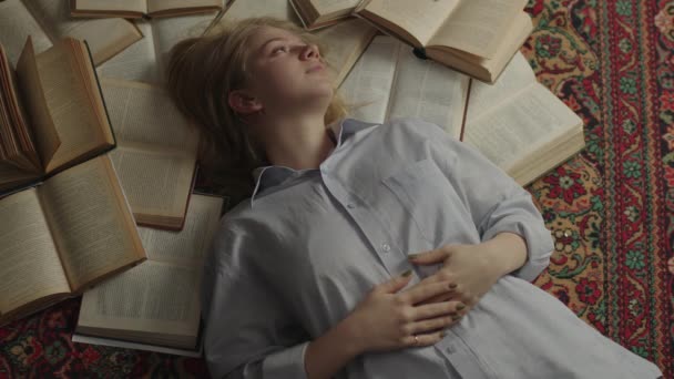 Millennial kvinna ligger på golvet full av öppna böcker och drömmer. Studerande känner sig trött och blundar i hög med böcker på mattan. — Stockvideo