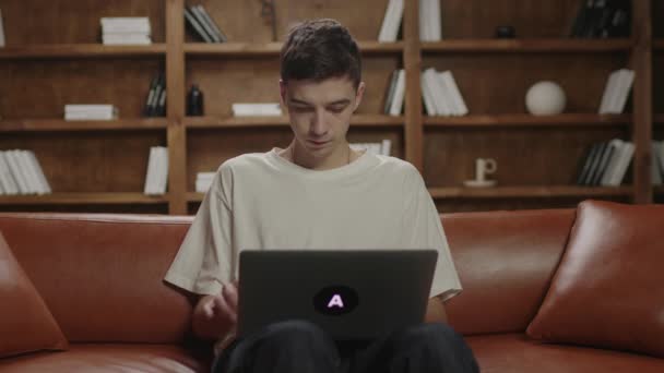 Jovem de 20 anos trabalhando homem usando laptop sentado no sofá. Freelancer masculino digitando no laptop, navegando na internet. Millennial estudando em casa. Trabalho e educação online. — Vídeo de Stock