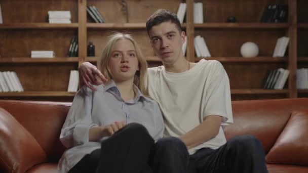 Casal Millennial assistindo filme assustador sentados juntos no sofá. Namorado e namorada abraçando na frente da TV. Família entretenimento noturno. — Vídeo de Stock