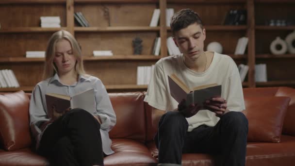 20多岁的夫妇坐在家里的沙发上看书。聪明的年轻人读文学。男人和女人都喜欢看书. — 图库视频影像