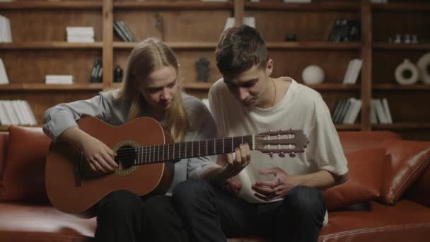 Chłopak uczy swoją dziewczynę grać na gitarze. Młody mężczyzna i kobieta grający na gitarze. Para uczy się grać na instrumencie muzycznym. — Wideo stockowe