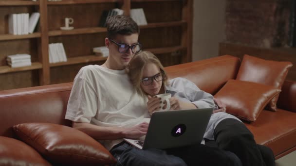 Millennial coppia guardando film o spettacolo sul computer portatile seduti insieme sul divano. Fidanzato e fidanzata che si abbracciano. Animazione serale familiare. — Video Stock