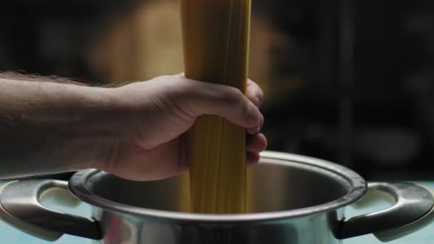 Mano masculina lanzando pasta de espaguetis en agua hirviendo. Vista lateral de la pasta en sartén en cámara lenta. — Vídeo de stock