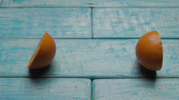 Оранжевые половинки фруктов падают на синий стол. Сочные цитрусовые на деревянной доске. — стоковое видео