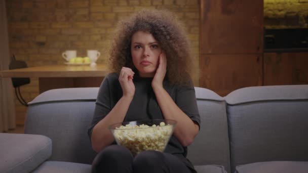 Mujer milenaria viendo películas de miedo sentada sola en el sofá con maíz pop. Mujer asustada viendo la televisión y asustarse de repente. — Vídeos de Stock