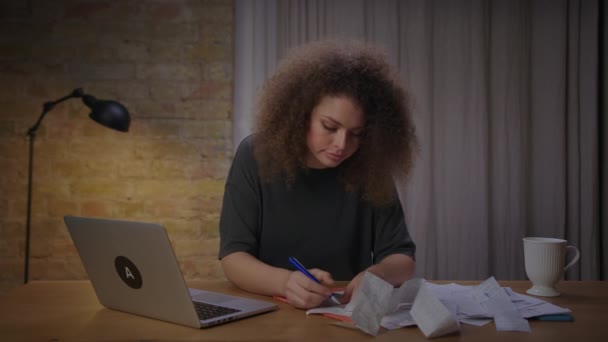 Millennium-Frau prüft Spesenrechnungen und macht sich Notizen am Laptop am Tisch. Haushaltsführung im eigenen Land. — Stockvideo