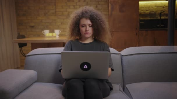 Studentessa adulta che impara da casa usando il portatile seduta sul divano. Giovane donna digitando sul computer portatile che lavora a casa. — Video Stock