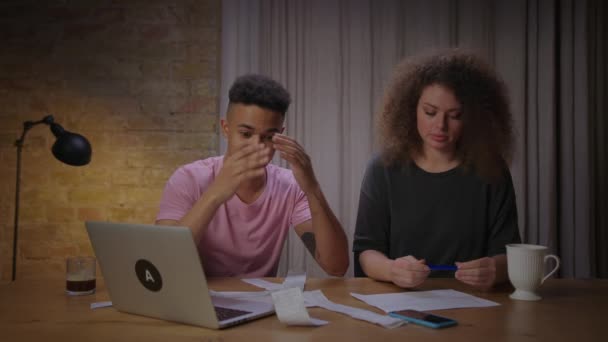 Millennial multiethnic couple managing family expenses with paper bills and bank documents on the table. African American boyfriend accounting family costs with his girlfriend. — Stock Video