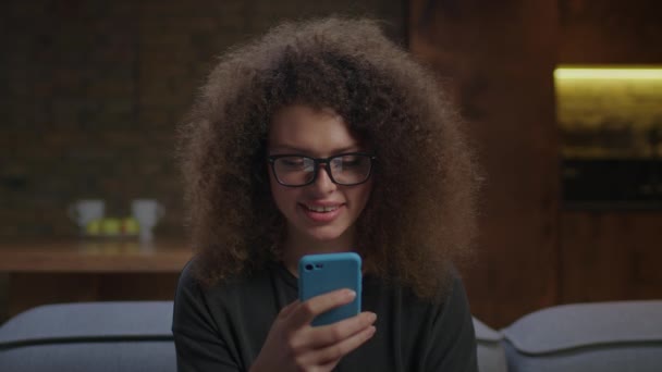 20s mulher encaracolado em óculos de olho navegar na web usando telefone móvel. Close up de mulher milenar navegando na internet no telefone celular em casa. — Vídeo de Stock