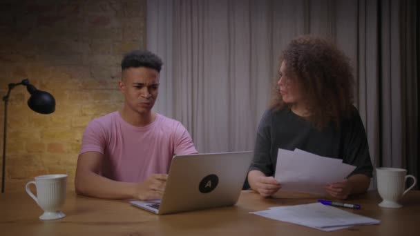 Jovem afro-americano procurando emprego e tendo entrevista online e namorada mostrando-lhe dicas e respostas certas. Casal de raça mista batota com vídeo chamada entrevista. — Vídeo de Stock