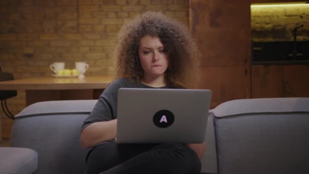 Een jonge vrouw die een trieste film kijkt op een laptop die alleen thuis op de bank zit. 20s vrouw met behulp van laptop 's avonds voor huishoudelijk entertainment. — Stockvideo
