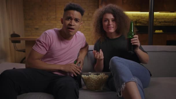 20s gemengde race familie geniet van het kijken naar voetbalwedstrijd op tv met popcorn en bier zitten op de bank. Afro-Amerikaanse mannelijke voetbal fan en zijn vriendin vieren overwinning doel van favoriete team. — Stockvideo