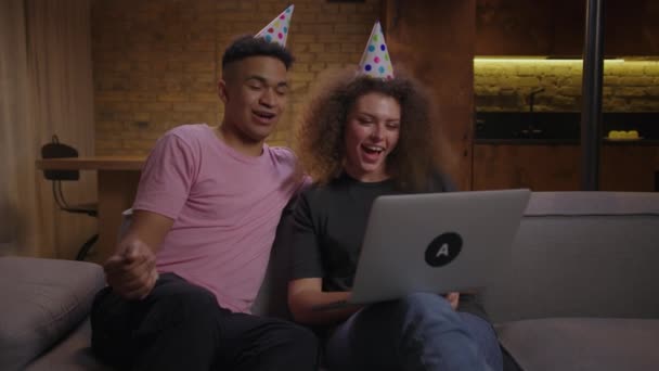 20s multiethnic couple congratulating friend with birthday talking to laptop. Young adults wearing party hat singing happy birthday song by video call. Birthday party online. — Stock Video