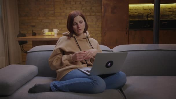 30s obchodní žena mluví videohovory pomocí notebooku sedí na gauči pracuje doma. Mladá dospělá žena má online konferenci z domova. — Stock video