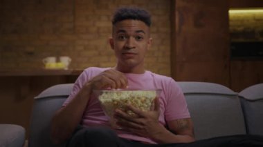 20 'li yaşlarda Afro-Amerikalı bir adam komedi programı izlerken gülüyor, kanepede oturmuş kamerada patlamış mısır yiyor. Erkek, büyük bir kase patlamış mısırla komik film izlemeyi sever..