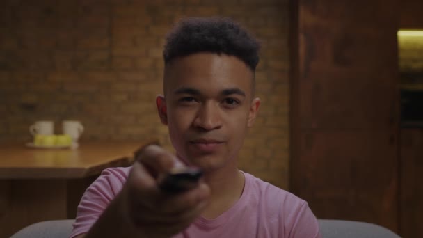 Millennial Afro-Amerikaanse man kijken spannende film of tv-show en het eten van popcorn zitten op de bank thuis. Close-up van de jonge volwassen man schakelen van TV met afstandsbediening. — Stockvideo