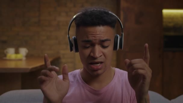 Joven adulto afroamericano hombre en auriculares con los ojos cerrados disfruta escuchando música favorita y cantando fuerte en cámara lenta. — Vídeo de stock