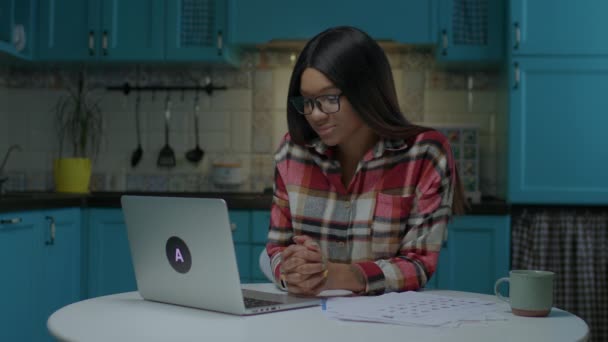 Millennial Afroamerikanerin spricht per Videotelefon am Laptop und trinkt Kaffee, der zu Hause am Küchentisch sitzt. Hübsche junge Dame spricht mit Freund online. — Stockvideo