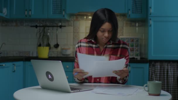 20s estudiante afroamericana mujer que trabaja con documentos en papel y portátil para la tarea en línea. Joven empresaria que trabaja con papeles en casa. — Vídeo de stock