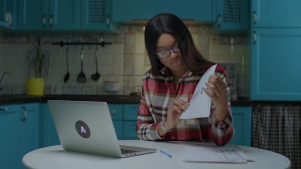 Jeune enseignante afro-américaine en ligne dans des lunettes parlant et montrant une feuille de papier avec des lettres ABCDE regardant un ordinateur portable. Enseignant préscolaire travaillant à distance de la maison. — Video